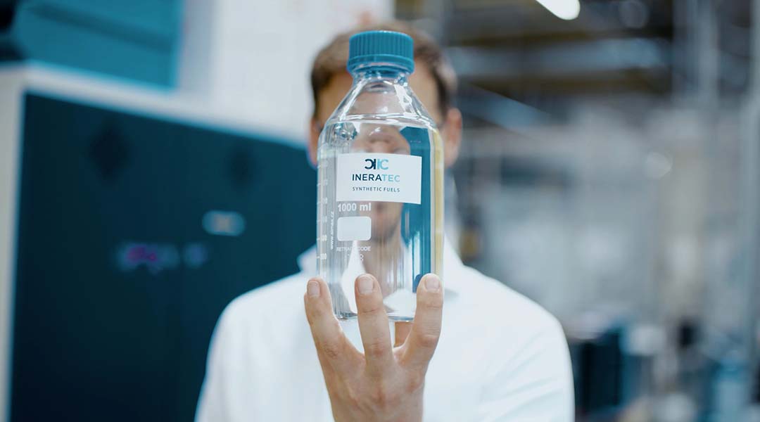 A man holding a glass jar labelled INERATEC e-fuel