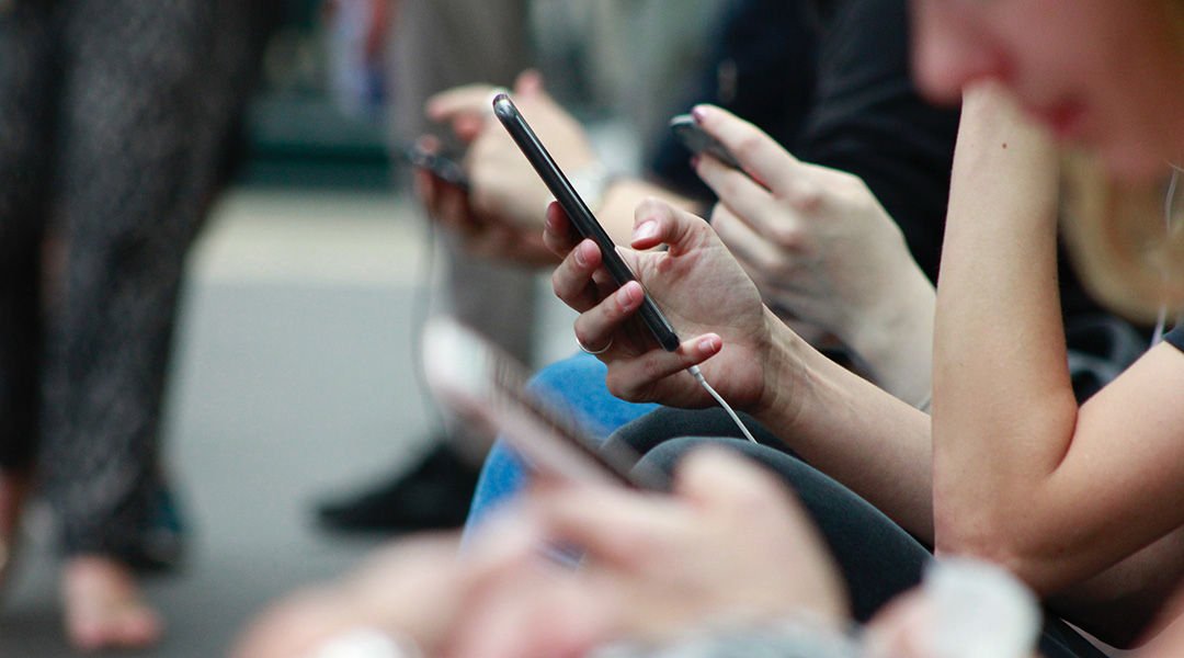 A line of people scroll through their phones on a subway.