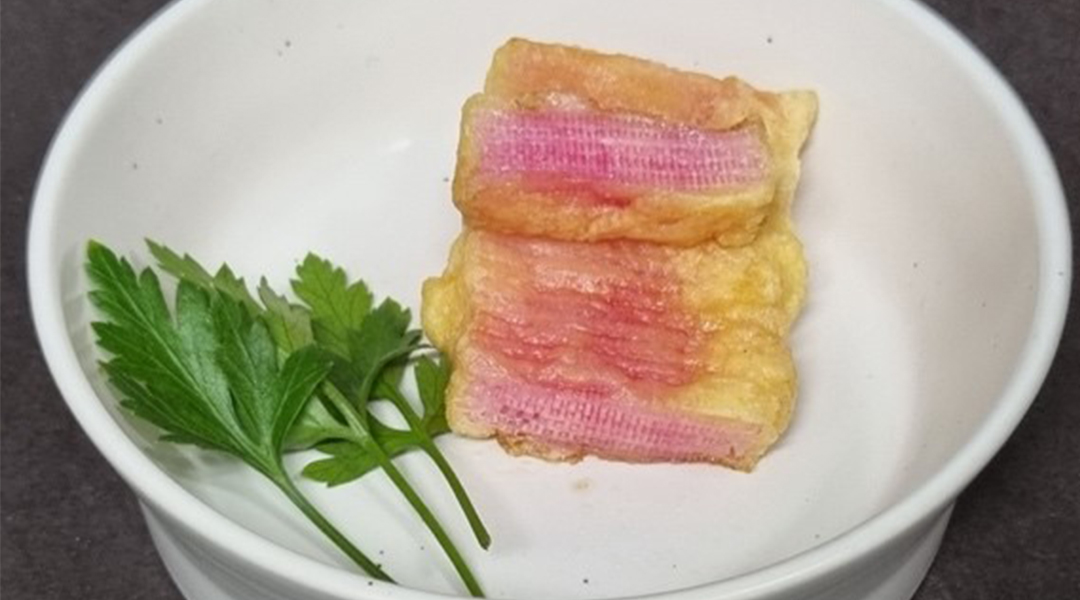 Several pieces of pink lab-grown steak with fat-laden microchannels on a white plate next to a garnish of parsley.