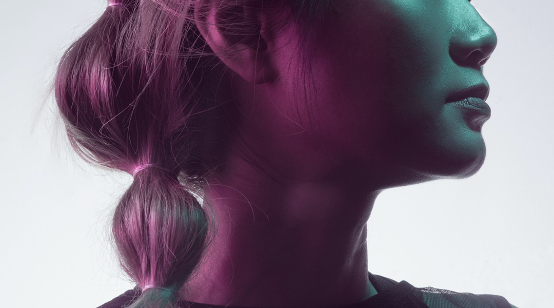 Side profile of a woman's face under pink and green lighting.