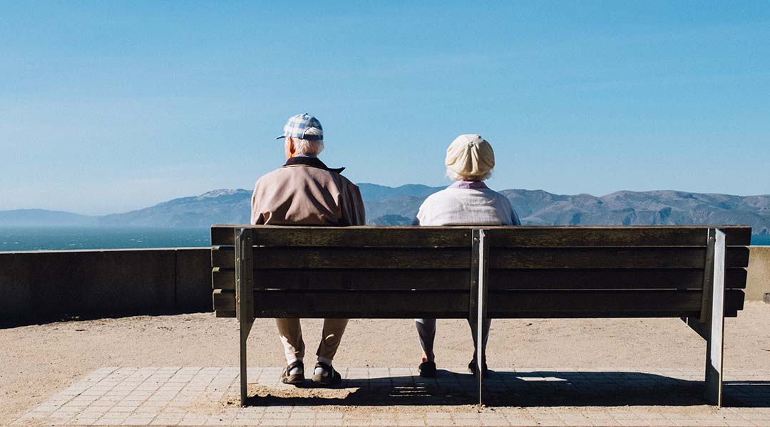 An elderly couple sitting on a bench.