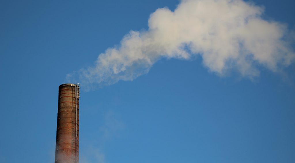 A smoke stack emitting a white gas against blue sky.