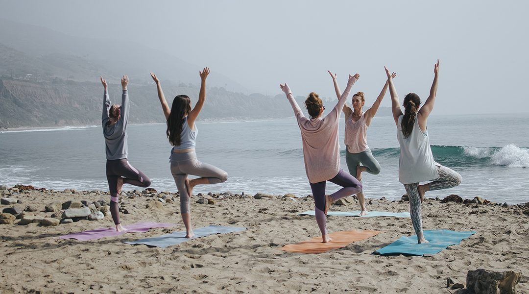 Five women on a beach doing yoga