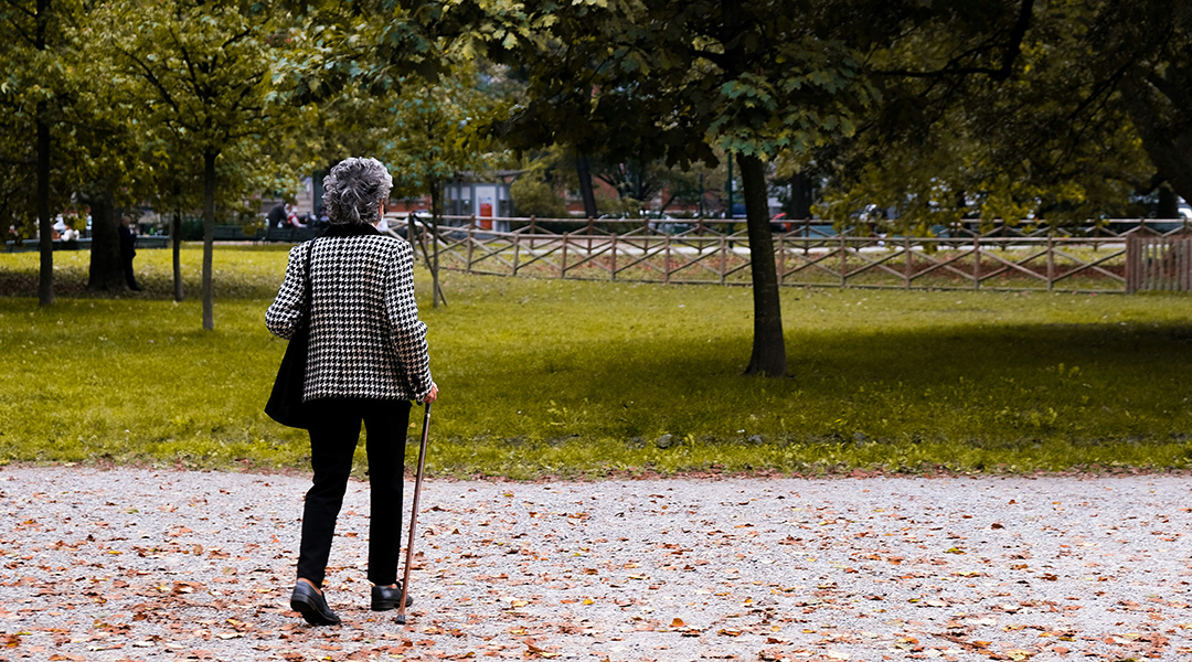 An elderly woman walking through a park.