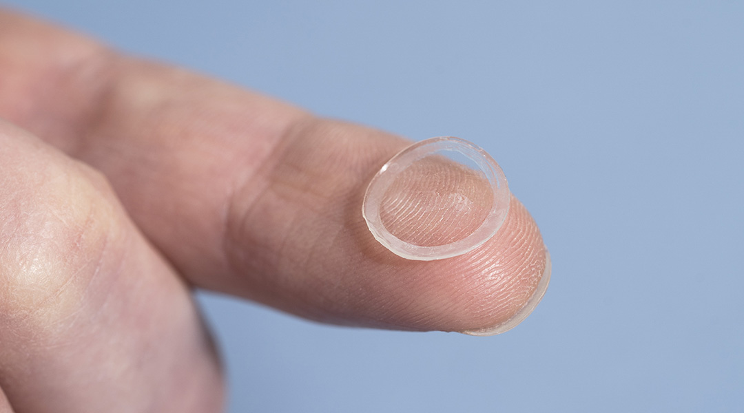 A self-lubricating contact lens held on a fingertip.