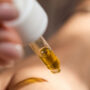 A person holding a dropper filled with yellow liquid over their skin.